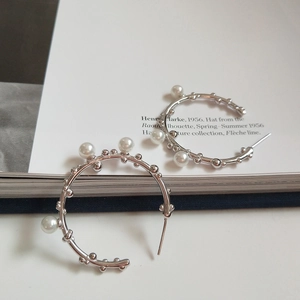 Detail of silver C-shaped earrings with white pearls and textured metallic beads