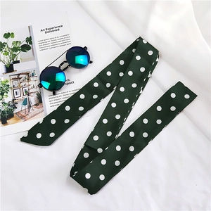 Detailed view of long green silk scarf with white polka dots on a magazine backdrop