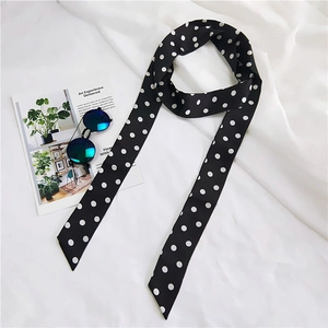 Detailed view of long polka dot skinny scarf on white fabric with fashion accessories