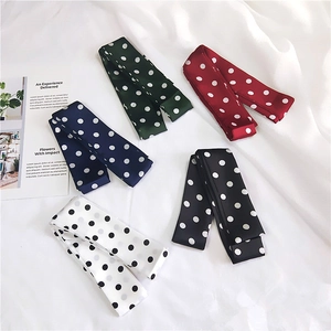 Polka dot skinny scarves in various colors laid flat on white fabric background