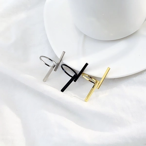 Dettaglio di tre anelli geometrici minimalisti nelle finiture argento, nero e oro