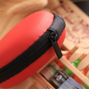 Close-up of a small red EVA storage pouch with black zipper on a wooden table