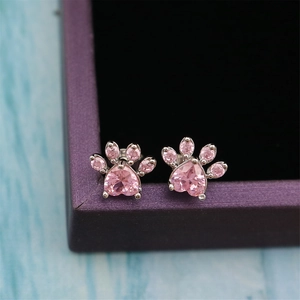 Close-up of pink zircon cat paw stud earrings resting on a purple jewelry gift box