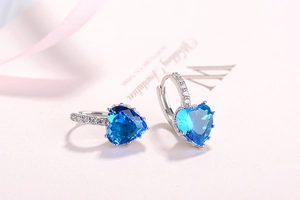 Macro shot of silver heart hoop earrings with blue zircon on a pink wedding card