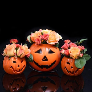 Three orange Halloween pumpkin lanterns with vivid roses on a black reflective surface