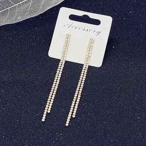 Detailed view of long gold tassel earrings with sparkling rhinestones on a blue background