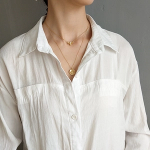 Close-up of a layered gold necklace set featuring a bee and textured round coin pendant