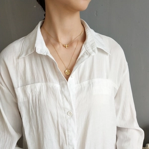 Close-up of a double-layer gold bee and hammered disk pendant necklace on a model