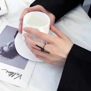 Dettaglio di un anello geometrico nero aperto indossato tenendo una tazza da caffè bianca