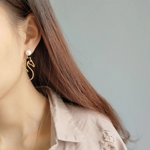 Detailed close-up of a gold horse head earring with a white pearl on a female model