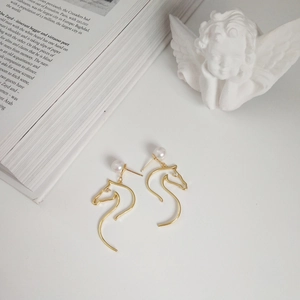 Detail of horse-shaped pearl stud earrings in gold finish with minimalist aesthetic