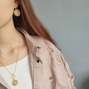 Model wearing gold embossed pendant necklace and matching openwork pattern earrings