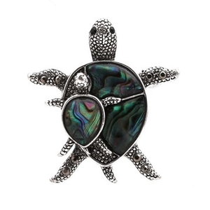 Macro detail of a silver turtle brooch featuring iridescent abalone shell inlay