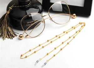 Close-up of golden eyeglass chain with oval beads and stylish oversized gold-rimmed glasses