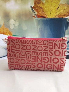 Detail of beige woven pouch with red SOIGNE jacquard lettering and zipper closure