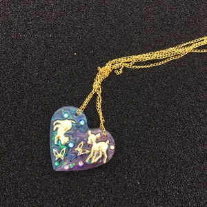 Gros plan d'un pendentif cœur en résine violette avec incrustations de cerf et papillon dorés