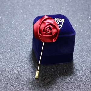 Macro detail of a red satin rose brooch with gold leaf on a blue velvet jewelry box