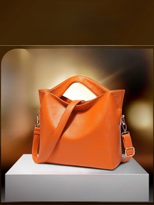 Detail of orange lychee textured leather handbag showing the grain and side buckles
