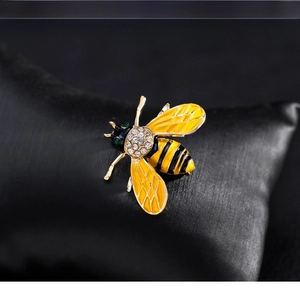 Detailed macro of crystal bee brooch with yellow enamel wings on black satin texture