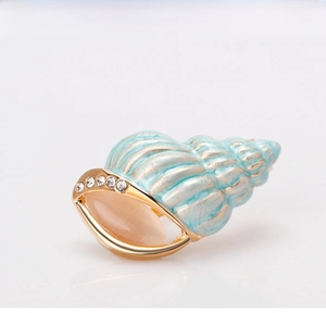 Detailed view of light blue conch brooch with gold edges and sparkling crystal stones