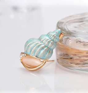 Detailed macro view of conch brooch with light blue enamel and pink cat eye stone decoration