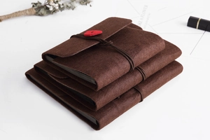 Three stacked brown felt DIY photo albums with red heart ties on a white desktop