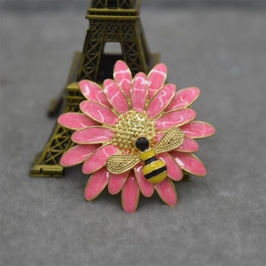 Detail shot of a pink daisy flower brooch with a small bee and enamel finish details