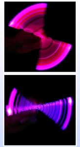 Close-up of spinning LED pen showing dynamic pink and purple light trails in the dark