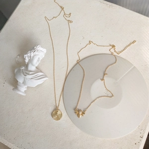 Close-up of gold bee and honeycomb pendants on fine chains over a textured stone surface