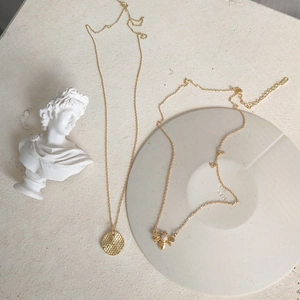 Detail of gold bee and honeycomb pendants on fine chains over artistic plaster decor