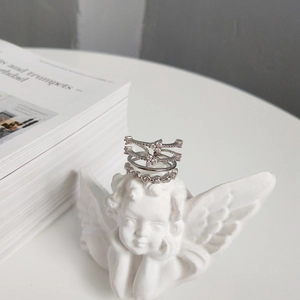 Artistic display of layered silver zircon rings on a white angel sculpture minimalist background