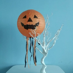 Close-up of orange Jack-o-lantern paper lantern with hanging ribbons on white branches