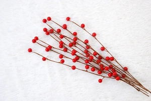 Close-up of artificial red berry branches for Christmas tree decor on white plush surface