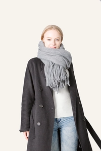 Front view of model wearing a thick grey scarf with long tassels over a black wool coat