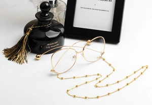 Detailed shot of gold metal glasses chain with beads on a minimalist white table
