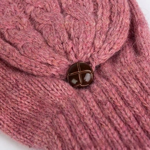 Détail de gant en laine rose tricoté avec motif torsadé et bouton décoratif marron