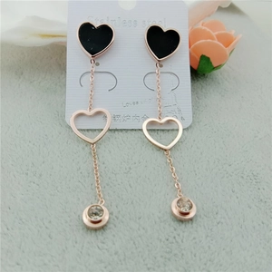Détail de boucles d'oreilles pompon en acier rose avec clou coeur noir et zircone cubique