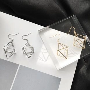 Macro shot of gold and silver hollow geometric asymmetric drop earrings on a dark background
