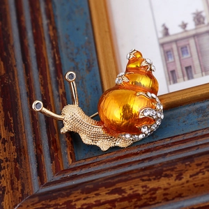 Macro detail of snail brooch with orange enamel shell and sparkling crystal accents
