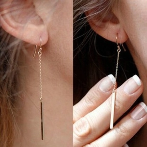 Close-up of golden asymmetric tassel earrings worn on ear with long pendant detail