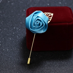 Close-up of blue fabric rose brooch with golden metal leaves on black surface