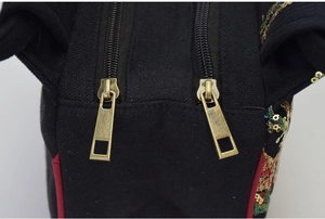 Close-up of bronze double metal zippers and peacock embroidery on black canvas bag
