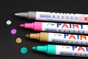 Detail of four colorful oil-based paint markers showing nib size and colors on black paper