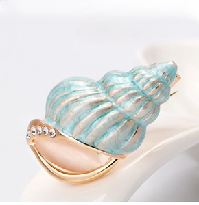 Detail of gold conch brooch with light blue enamel and pink cat eye stone inlay