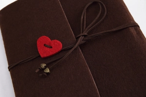 Close-up of brown felt DIY photo album featuring a red heart button and tie-string closure