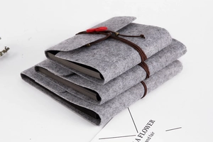 Three stacked grey felt DIY scrapbooks with brown leather cord and red heart detail