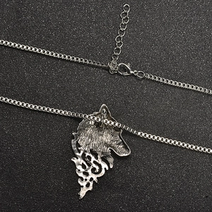 Detailed view of silver wolf head pendant with box chain and lobster clasp on dark surface
