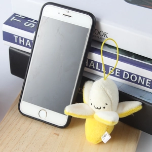Cute peeled banana plush toy with emoji face next to a phone for size scale