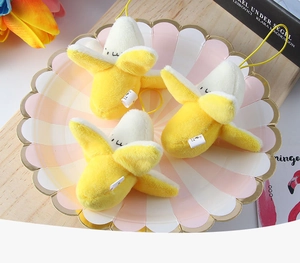 Three cute plush banana keychains with yellow straps displayed on a decorative paper plate