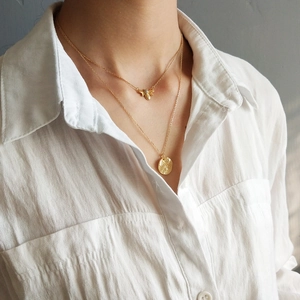 Close-up of a double-layered gold necklace with honeybee and hammered coin pendants